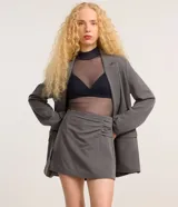 Short pollera corto color gris, de sastrería con cierre por cremallera invisible en la parte de atrás, pences y detalle en fruncido en el lateral.