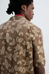 Camisa marrón con estampado floral, corte relaxed fit, cuello bowling, manga corta, bolsillo en el pecho, aberturas laterales y cierre con botones.