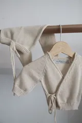 Conjunto tejido artesanal en hilado color crudo, compuesto por un cárdigan cruzado con lazos y un pantalón con cintura ajustable con lazos.