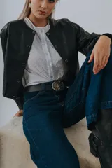 Campera bomber color beige de cuero, con cuello redondo, cierre frontal con botones a presión, mangas largas con puños elásticos y detalles de tachas metálicas en hombros y espalda.