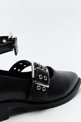 Zapato tipo zueco negro charol con punta fina, doble tira con hebillas metálicas y pulsera al tobillo con tachas.