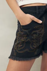 Short de jean azul con bordado floral en el frente y ruedo desflecado.