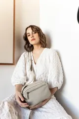 Bandolera rectangular de cuero color nude con doble compartimento con cierre de cremallera plateada y correa de cuero ajustable.