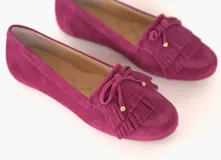 Mocasín de cuero gamuzado color fucsia, con flecos en la capellada y un lazo con herrajes metálicos dorados. Interior forrado en cuero y suela de goma flexible.