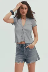 Camiseta color beige de tejido de punto, con cuello halter y escote pico. Tiene cierre frontal con botones y mangas cortas.
