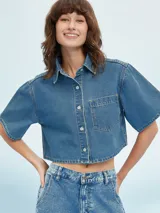 Camisa de manga corta color celeste, con cuello clásico, cierre frontal con botones y bolsillo de parche en el pecho.