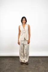 Pantalón de vestir color crema, de corte recto y tiro alto, confeccionado en lino. Presenta bolsillos laterales y cierre frontal con botón y cremallera.