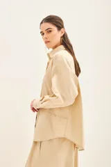 Camisa beige de poplin amplia, con botones laterales para abotonar de forma cruzada.