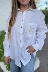 Camisa blanca de lino con botones y bolsillo en el pecho con bordado de letras.