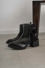 Bota corta de cuero marrón con puntera redondeada y taco cuadrado. Presenta una correa con hebilla alrededor del tobillo y cierre lateral.