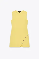 Vestido corto amarillo de punto, con cuello redondo, sin mangas y botones metálicos irregulares en el lateral.