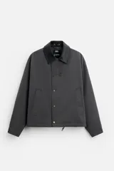 Cazadora relaxed fit color gris oscuro, confeccionada en tejido técnico repelente al agua. Tiene cuello solapa de cuero negro, manga larga con puños ajustables, bolsillos de vivo en la cadera, bolsillo interior, bajo ajustable con cordón y cierre frontal con cremallera oculta por solapa con botones.