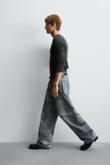 Pantalón de jean azul con efecto lavado y estampado, corte holgado y amplio en toda la pierna, tiro medio, cinco bolsillos y cierre frontal con cremallera y botón.