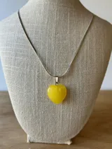 Collar con cadena plateada y dije de corazón amarillo.