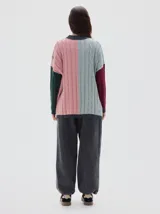 Buzo tejido colorblock con cuello subido tipo polera, diseño oversized y largo con pequeños cortes laterales. Presenta bloques de color rosa, celeste, bordó y verde oscuro, con cuello, puños y dobladillo en gris oscuro.