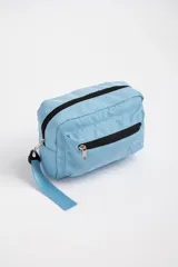 Necesser celeste rectangular de tela acolchada, con cierre superior y bolsillo frontal con cierre. Tiene una correa de mano en un lateral.