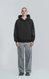 Hoodie negro de corte oversize con capucha, bolsillo tipo canguro y detalle de bolsillo con cierre en la manga izquierda.