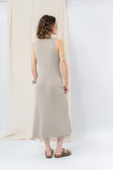Vestido midi color beige, de tejido tipo seda, con escote redondo, sin mangas y detalle de flecos en el ruedo.