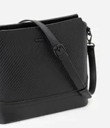 Bolso mediano tipo postman color negro con textura en relieve de líneas horizontales. Tiene correa larga regulable, cierre con cremallera y forro de poliéster.