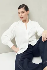 Camisa celeste de manga larga con cuello redondo y escote en V. Presenta detalles de pasamanería en el frente y las mangas, y botones forrados al tono. De corte fluido.