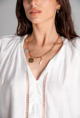 Collar dorado con cadena de eslabones grandes y dijes colgantes: avión, moneda, flor, placa con texto y dije celeste.