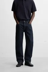 Jeans de corte slim fit confeccionados en denim de algodón sin lavados, color azul oscuro. Cierre frontal con botones y cinco bolsillos.