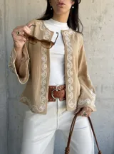 Chaqueta color beige con bordados blancos en el frente y las mangas, de corte recto y mangas anchas.
