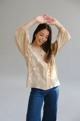 Camisa color beige con bordados florales blancos, cuello mao, mangas largas con elástico en los puños y cierre frontal con botones.