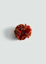 Accesorio para el pelo tipo scrunchie color rojo con ribete dorado y diseño de flor con textura.