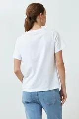 Remera blanca de algodón con estampado de flores rosadas y texto 'LET LOVE IN'.