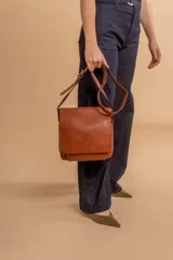 Bandolera de hombro color gris claro, con solapa frontal y correa ajustable. Presenta un diseño simple y práctico, ideal para uso diario.