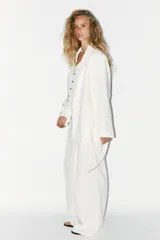 Blazer oversize color blanco confeccionado con 22% de lino. Tiene cuello solapa, manga larga con hombreras y abertura en la espalda. Incluye cinturón lazada en el mismo tejido.