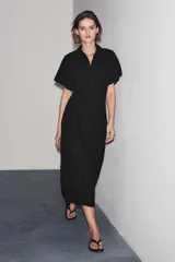 Vestido midi de algodón color negro, con cuello solapa, manga corta y falda evasé. Cierre frontal con botones y lateral con cremallera oculta.