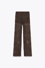 Pantalón semitransparente color marrón chocolate, de tiro medio y corte recto. Presenta aplicación de abalorios y lentejuelas plateadas con motivos geométricos y florales. Incluye short interior a tono.