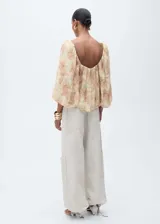 Blusa corta de gasa color crema con estampado floral en tonos durazno y verde. Tiene escote cuadrado, mangas largas abullonadas y espalda abierta.