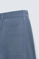 Pantalón de hombre color azul grisáceo, estilo balloon fit, confeccionado en mezcla de algodón y lino. Presenta pliegues en el delantero, cierre frontal con botón y cremallera, bolsillos laterales y bolsillos traseros de plastrón.