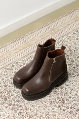 Botines negros de cuero con caña baja, puntera redondeada y cierre frontal con cremallera. Presentan paneles laterales de gamuza y suela track con plataforma.