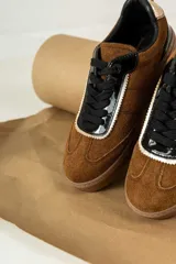 Championes marrones de cuero con cordones negros, puntera de charol y detalles dorados.