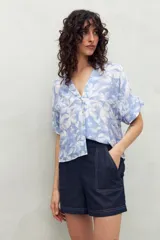 Camisa de manga corta con estampado de hojas blancas sobre fondo celeste, cuello solapa y botones de nácar al frente. Confeccionada en tejido liviano de sutil textura.