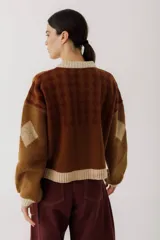 Cárdigan marrón con diseño de rombos en tonos rojizos y beige. Tiene cuello redondo, cierre frontal con botones y mangas largas con puños acanalados.