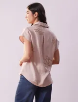 Camisa color beige con estampado de hojas marrones, de manga corta, con cuello a la base con solapa y escote en V.