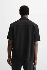Camisa color crudo de corte regular fit, confeccionada en tejido con textura. Tiene cuello bowling, manga corta, bajo con aberturas laterales y cierre frontal con botones.