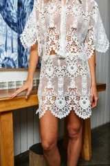 Falda corta blanca de encaje con diseño floral, corte evasé y cierre lateral.