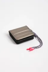 Billetera beige con diseño capitoneado y cierre de cremallera. Incluye cordón trenzado multicolor con terminales plásticas rosas.
