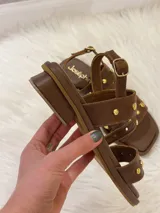 Sandalias bajas de cuero marrón con tiras cruzadas y apliques de tachas doradas.