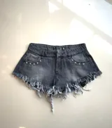Short de jean negro con efecto desgastado, tiro alto, corte ajustado, ruedo desflecado y apliques de estrellas metálicas en los bolsillos traseros.