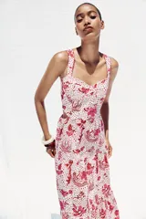 Vestido midi con estampado floral en tonos rosados, de escote recto y tirantes anchos con abalorios. Presenta aberturas laterales en la cintura y cierre trasero con cremallera oculta.