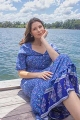 Vestido largo azul con estampado floral, escote en V, botones frontales, mangas cortas con volados y lazo ajustable en la cintura.