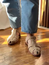 Sandalias de cuero color beige con diseño de tiras entrecruzadas y hebilla lateral.