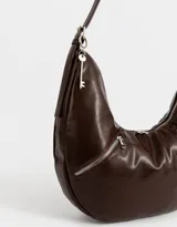 Cartera tipo saca color marrón oscuro de cuerina, con asa corta para el hombro, cierre superior y bolsillos frontales con cierre.